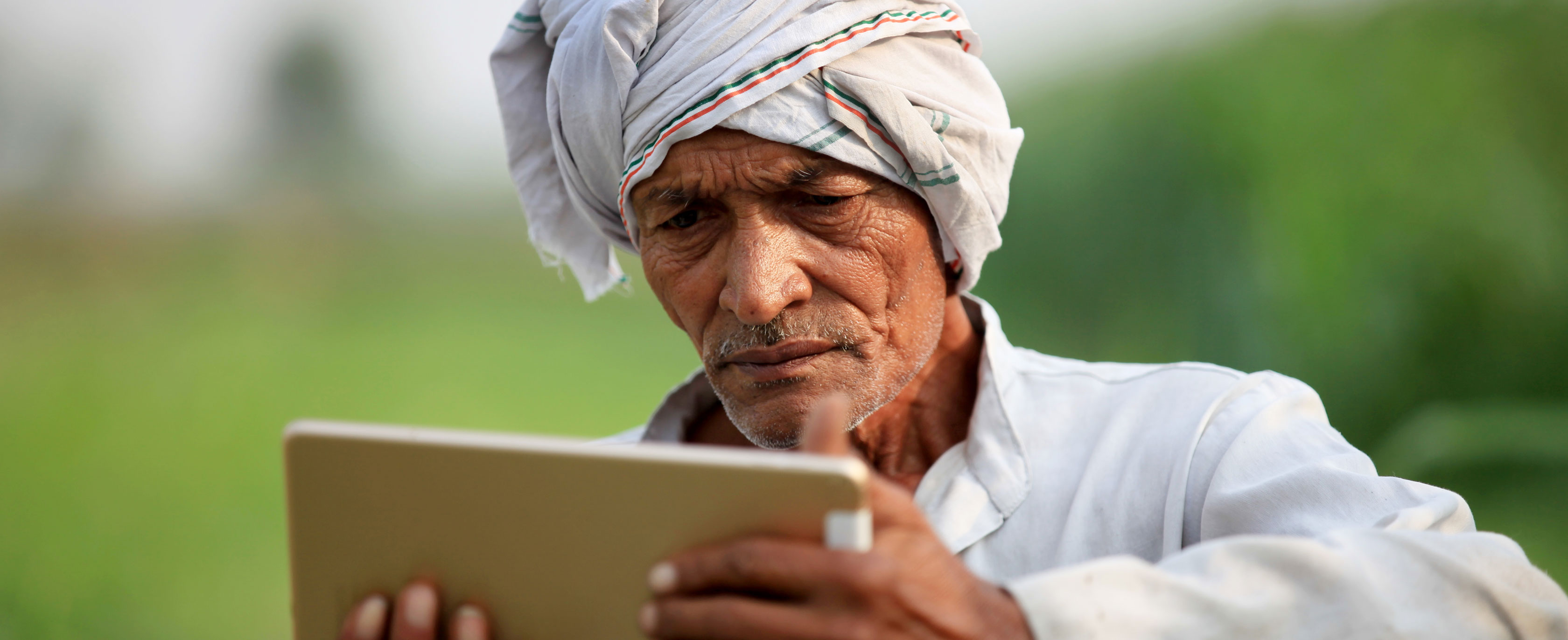 A man looks at a tablet in a field.