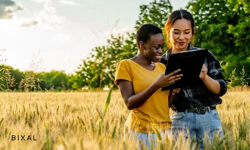 Two women stand in a field of tall grass looking at a tablet.