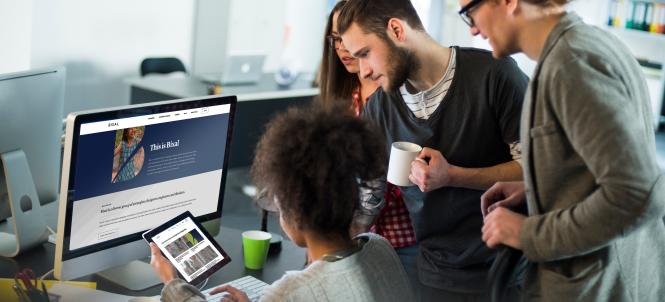 A group of people stand around a table looking at a computer screen.