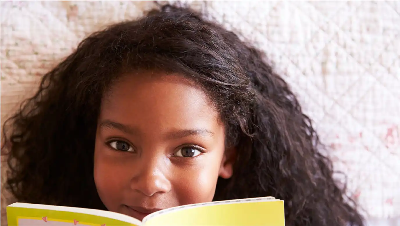 The face of a little girl peeking out behind an opened book.